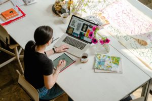 a person sitting at a table with a laptop and a drawing on it