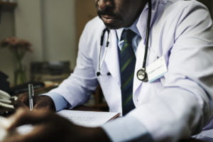 a man in a white coat and stethoscope sitting at a desk with a pen and