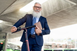 Senior business man going to work with electric scooter around city center
